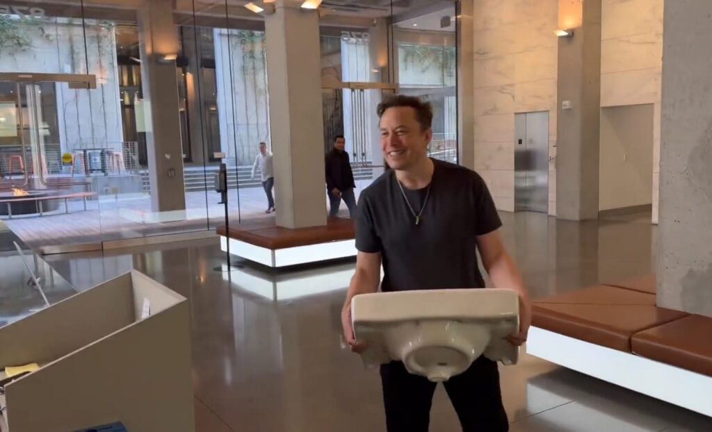 Musk dans le hall du siège de Twitter avec une vasque ou des toilettes dans les bras, l'air bête